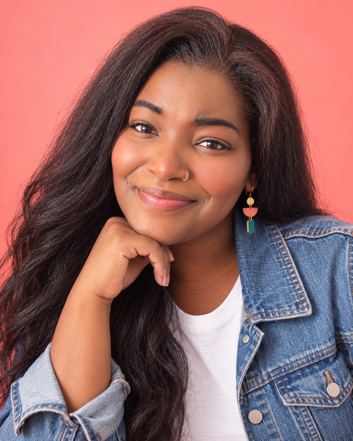 Diamond Simone smiling in a denim jacket against a coral backdrop.
